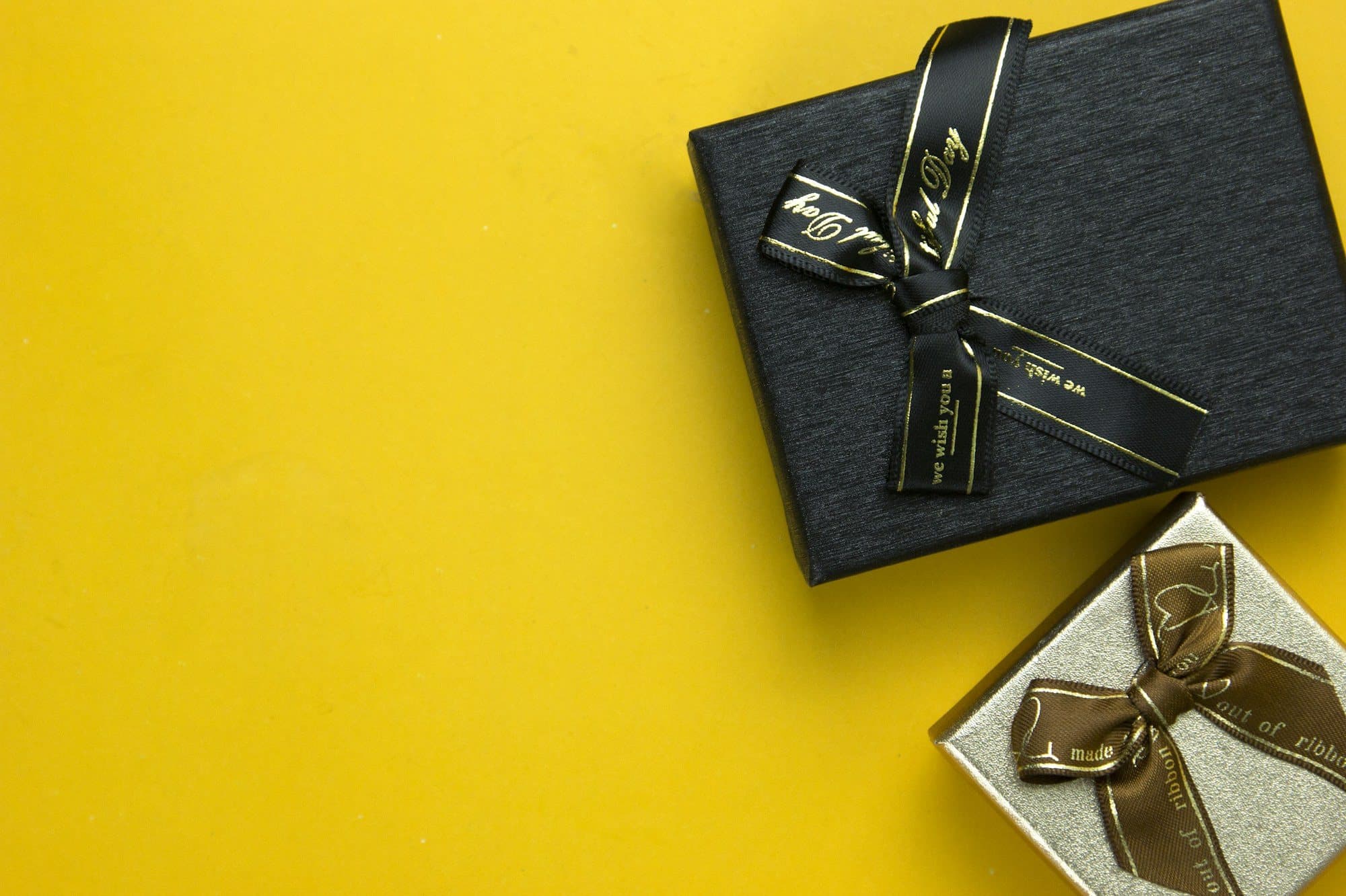 Black gift box tied with a gold ribbon on a yellow background