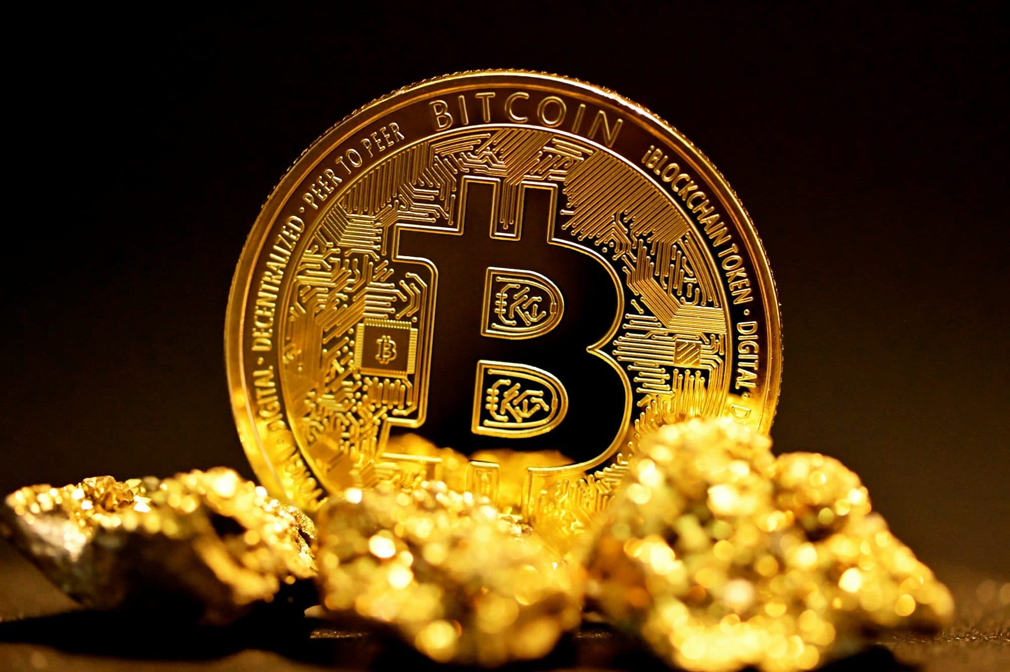 A gold bitcoin resting on a pile of gold nuggets